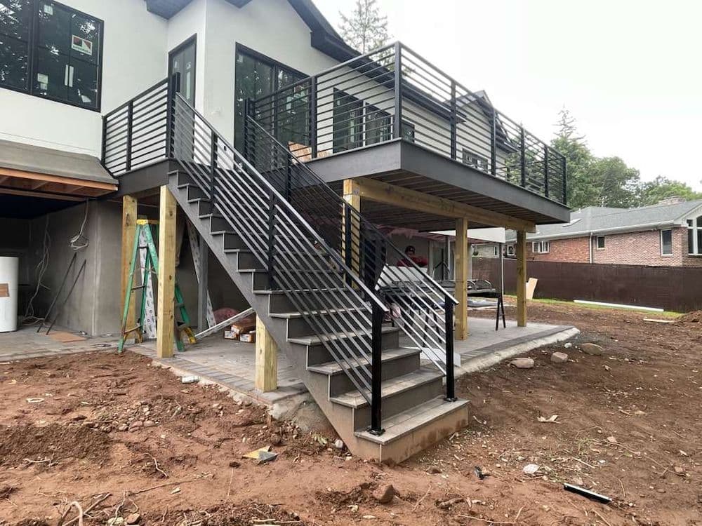 Modern elevated deck with black metal railing and stairs, surrounded by construction site.