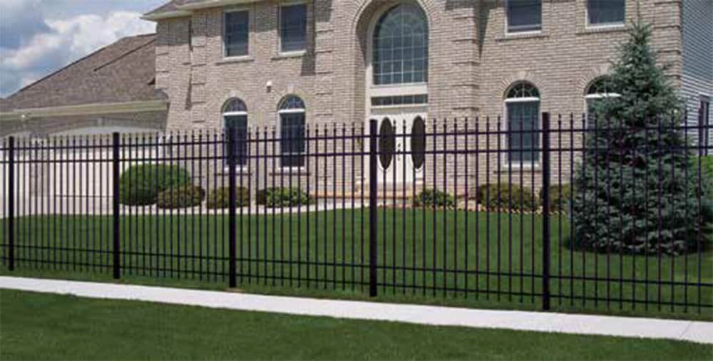 Black wrought iron fence in front of a modern brick house and well-maintained lawn.