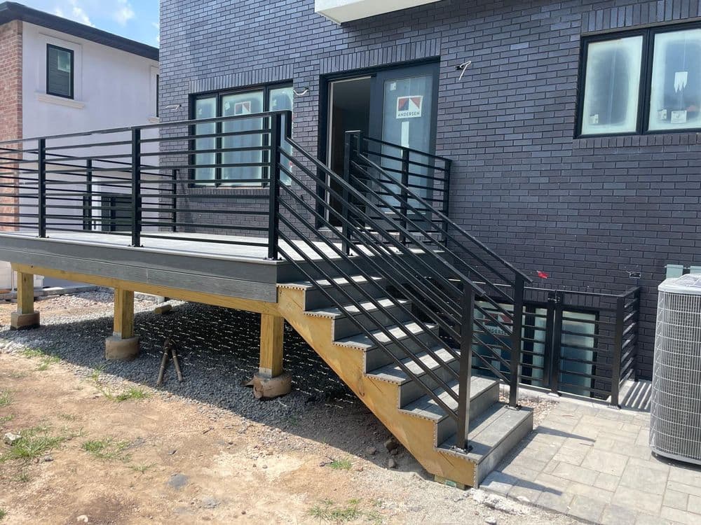 Black metal railing stairs leading to a modern building with brick exterior and gravel landscape.