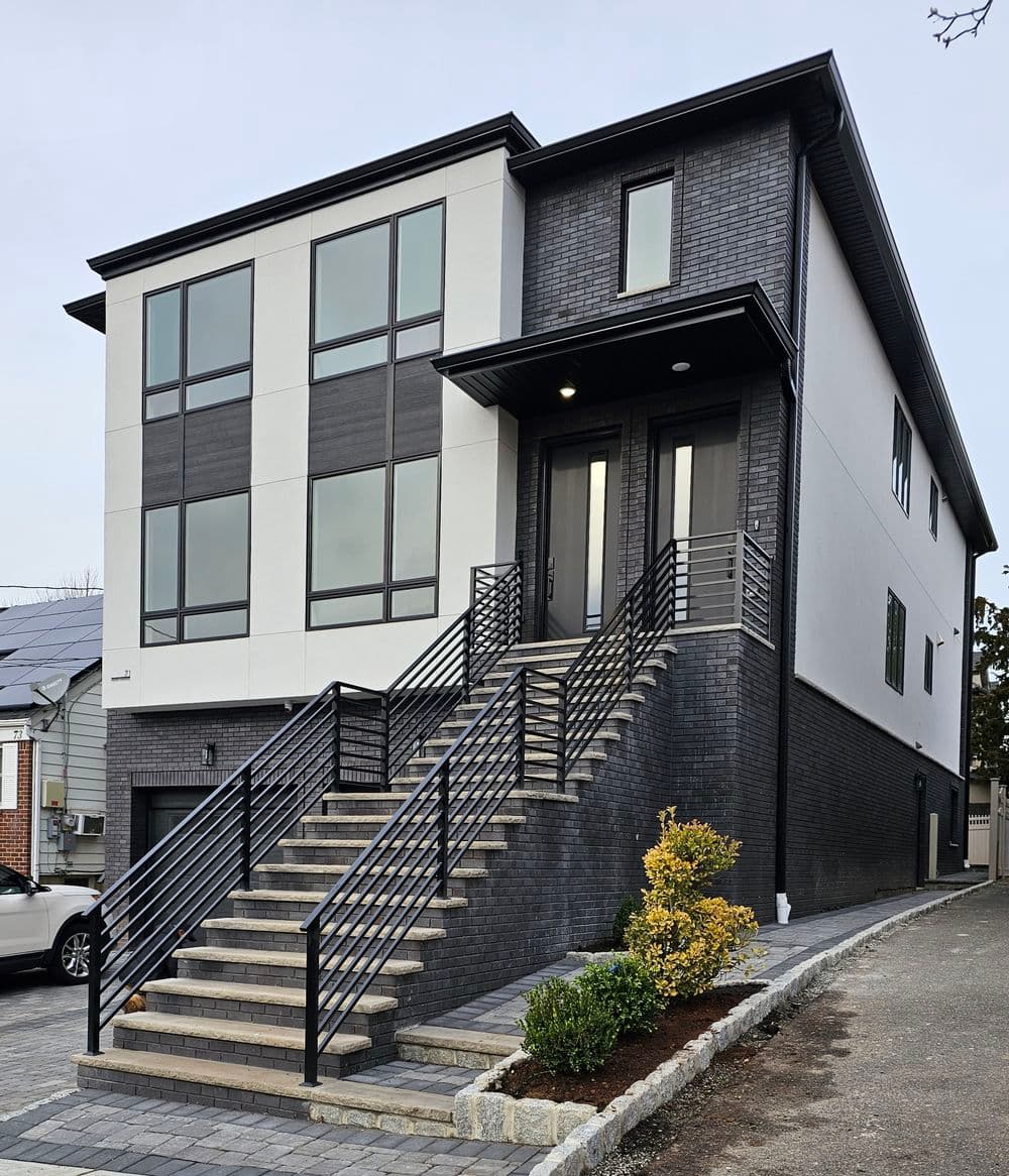 Modern two-story house with large windows, black accents, and a landscaped entrance.