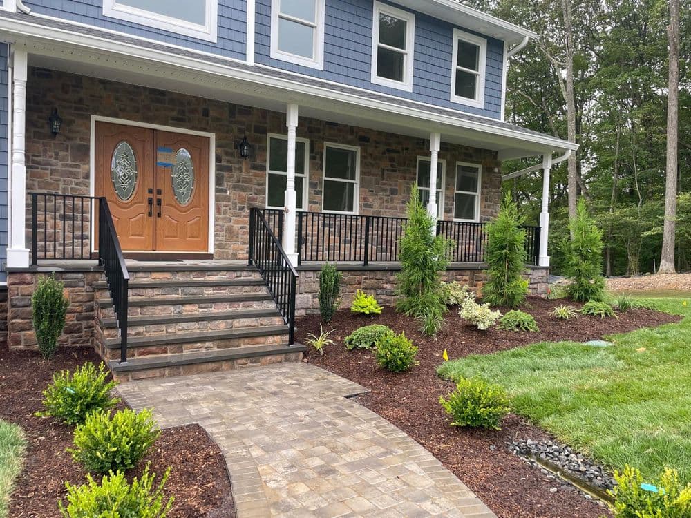 Elegant home entrance with stone steps, lush landscaping, and double wooden doors.