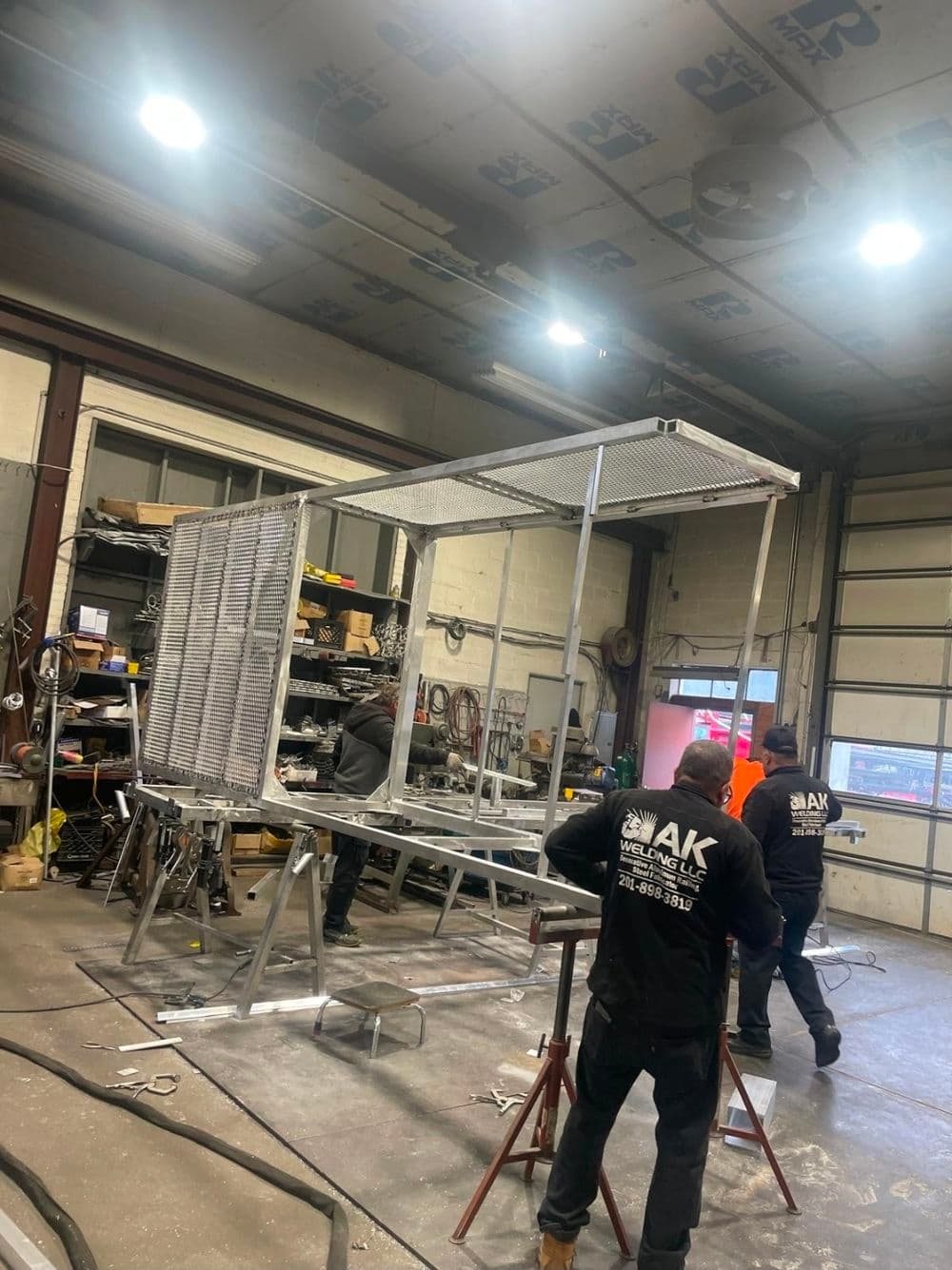 Workers constructing a metal frame in a workshop, showcasing industrial fabrication tools.