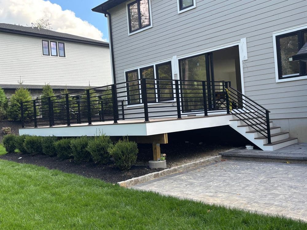 Modern outdoor deck with black railing beside a contemporary home and green grass.
