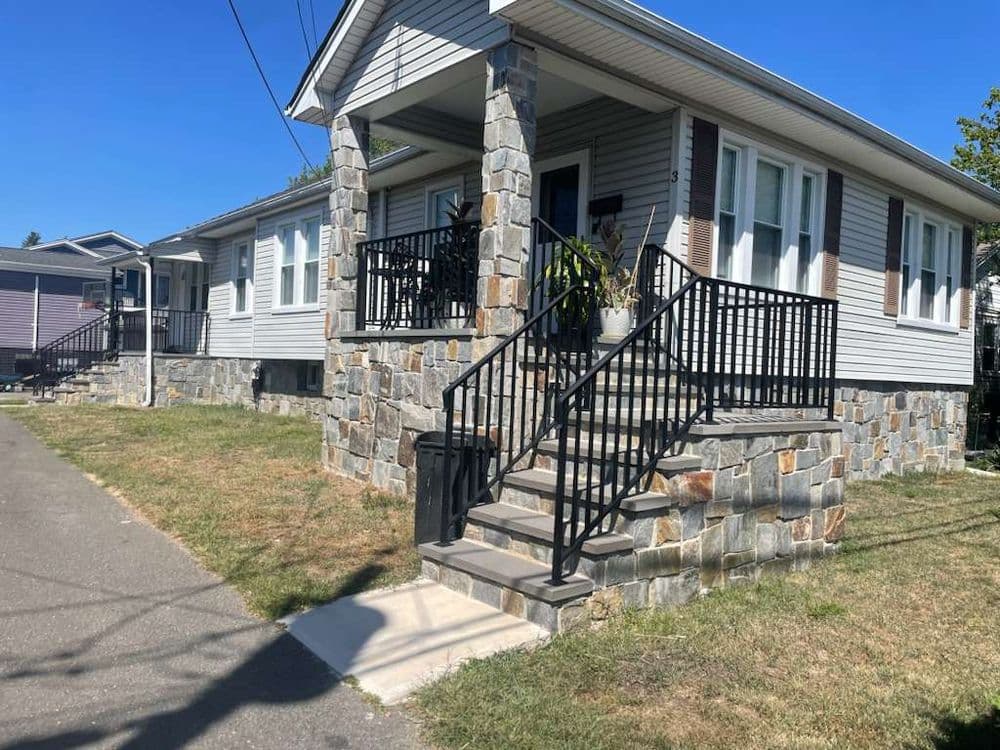 Charming house with stone steps and railing, surrounded by green grass and clear blue sky.