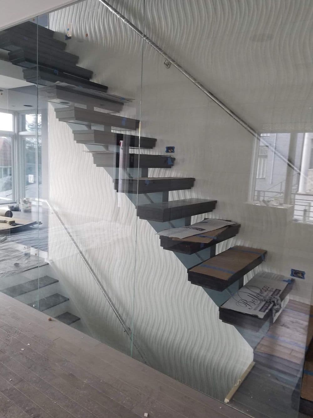 Modern glass staircase with wooden treads and wavy patterned wall in contemporary interior design.