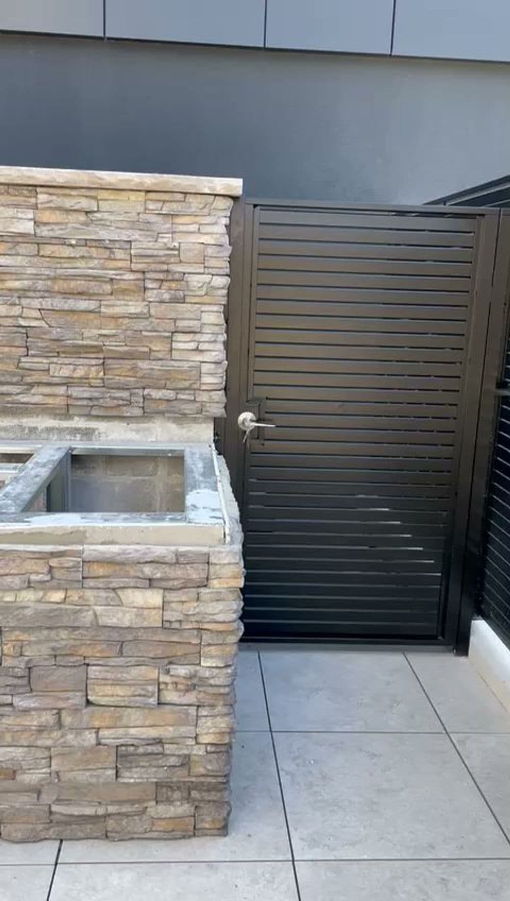 Modern outdoor kitchen with stone countertop and sleek black gate. Ideal for outdoor entertaining.