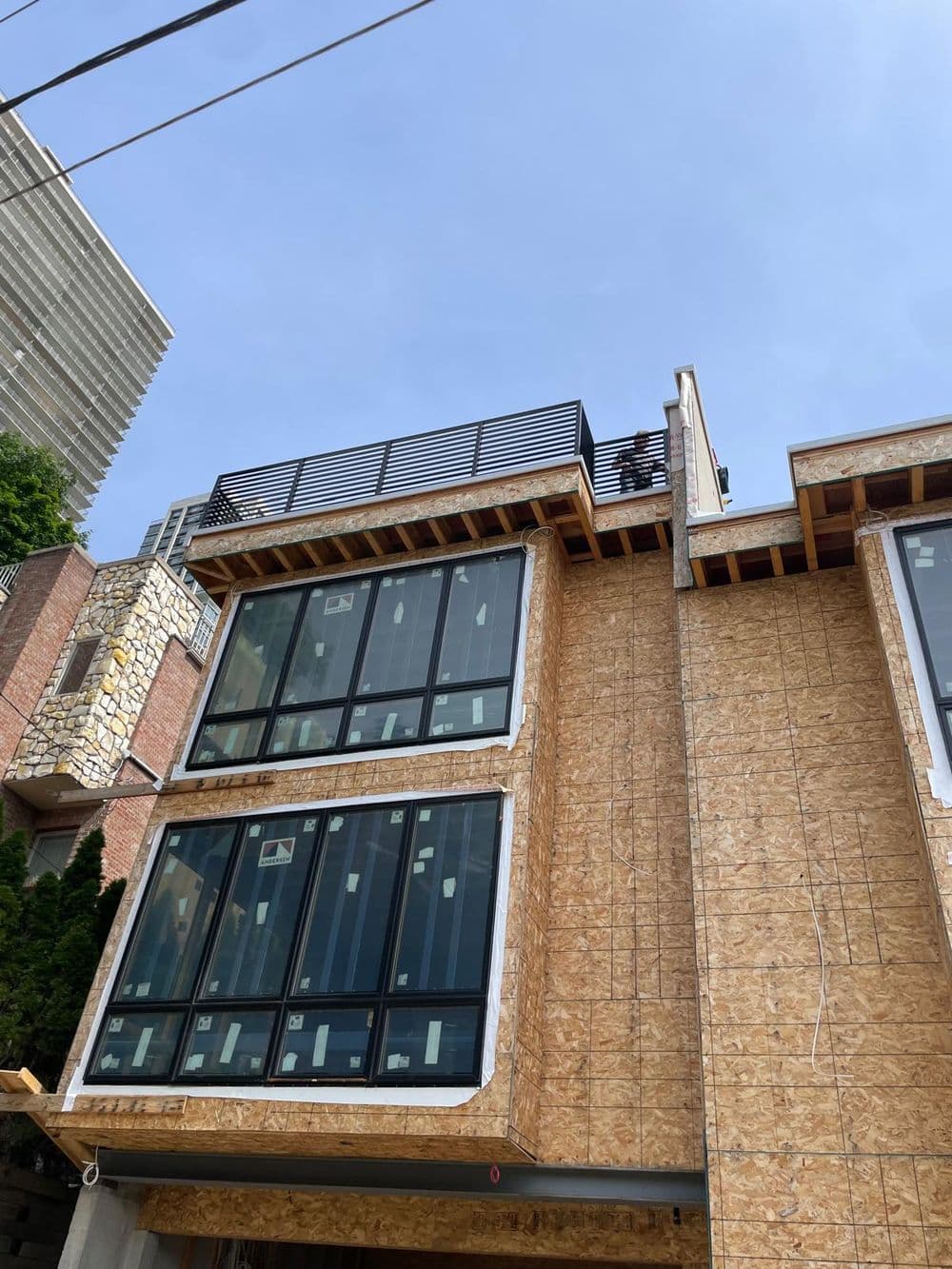 Modern building under construction with large windows and rooftop terrace. Clear blue sky above.