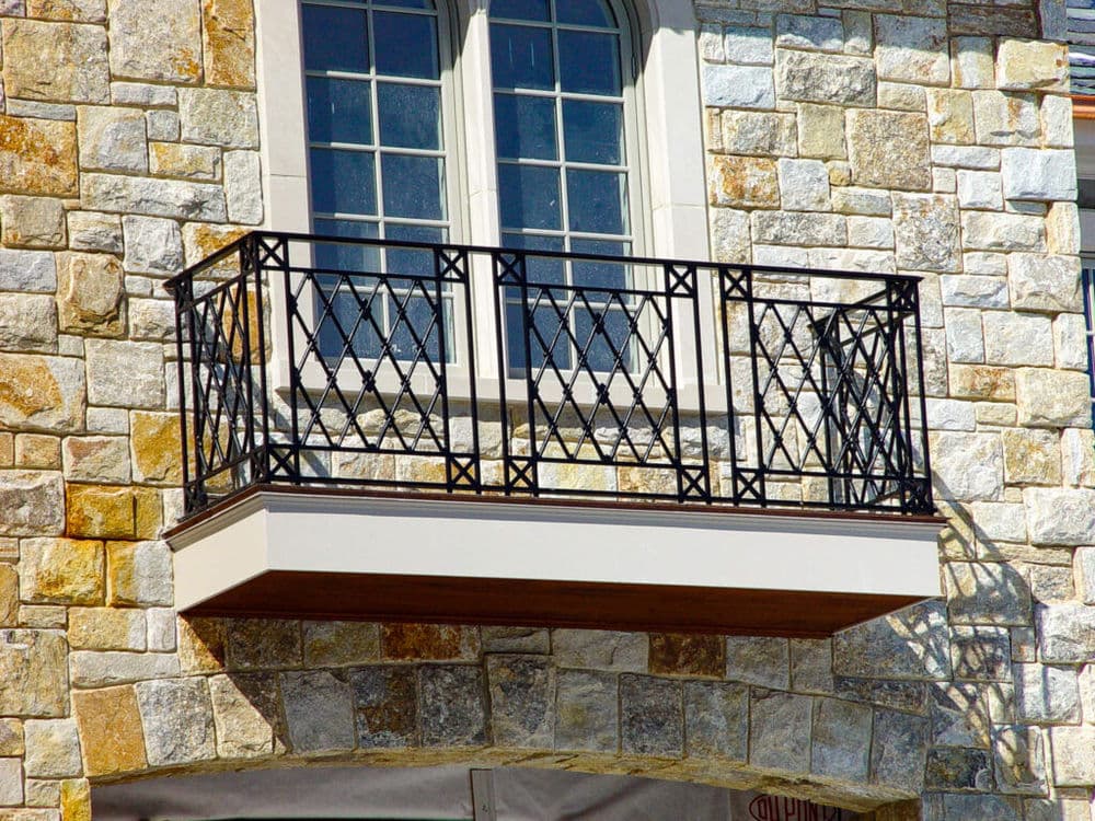 Stone building with decorative metal balcony and large window.