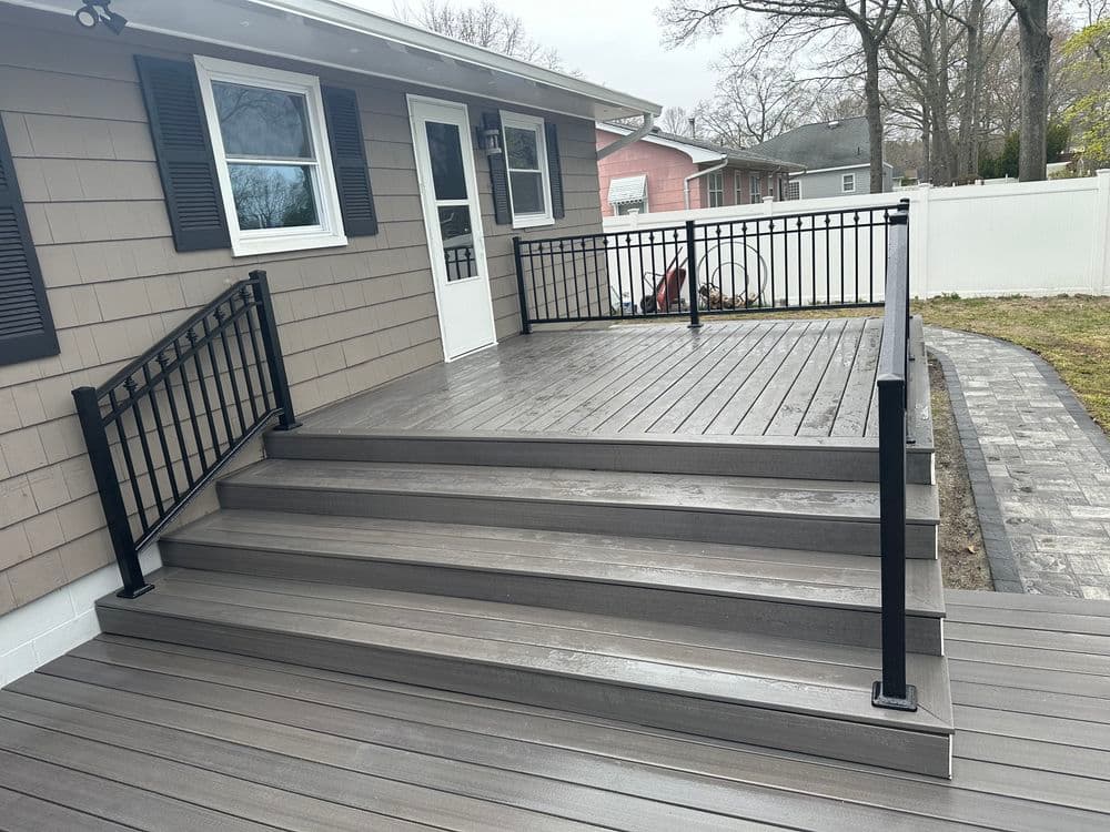 New gray composite deck with black railing and steps beside a modern house.