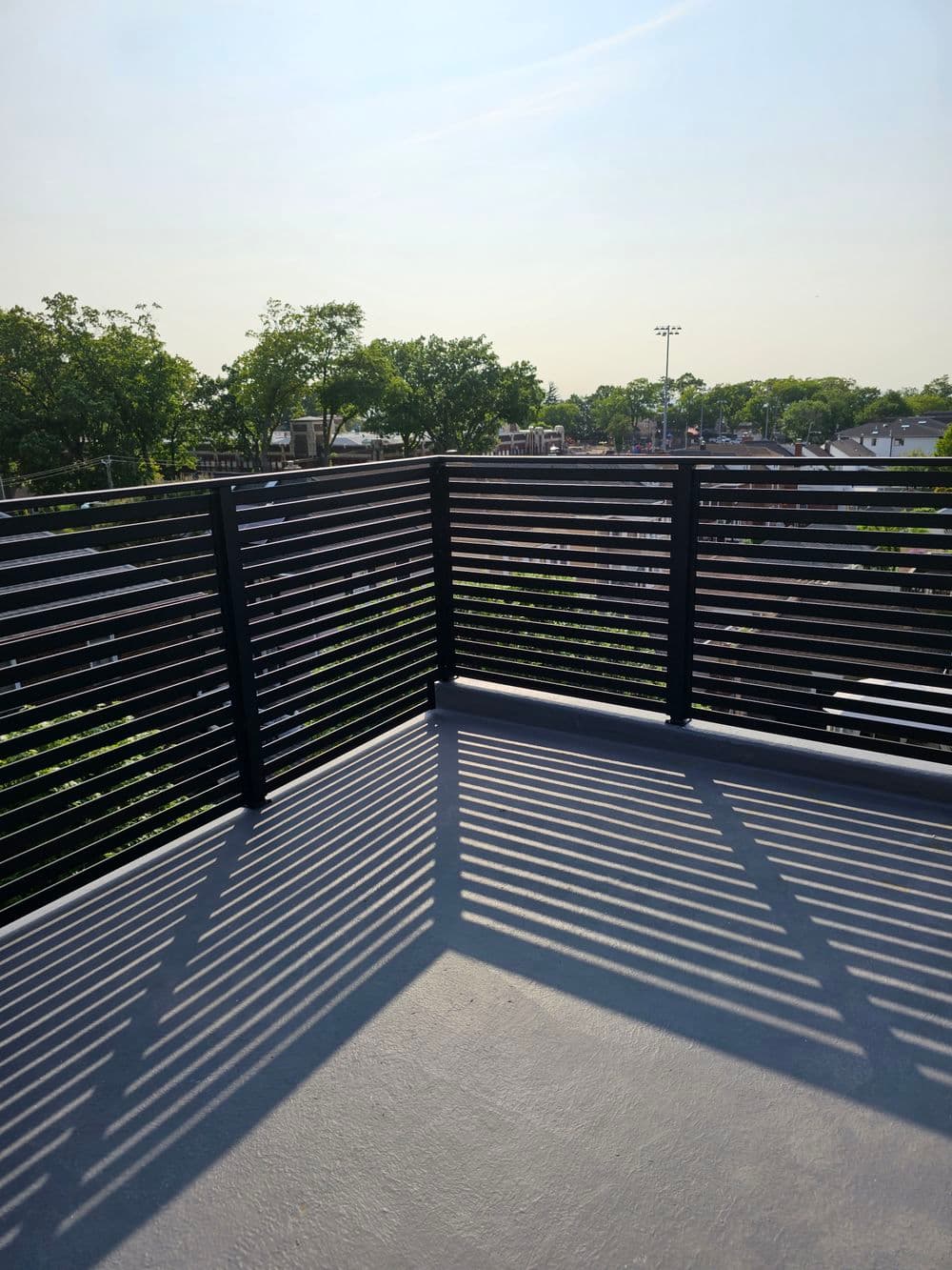 Rooftop balcony with sleek railings and sunlight casting long shadows on the floor.