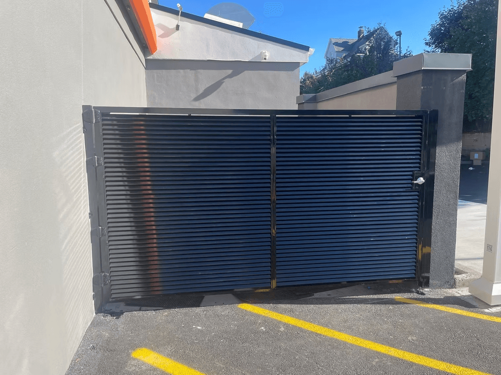 Black metal sliding gate at a commercial building entrance with clear blue sky.