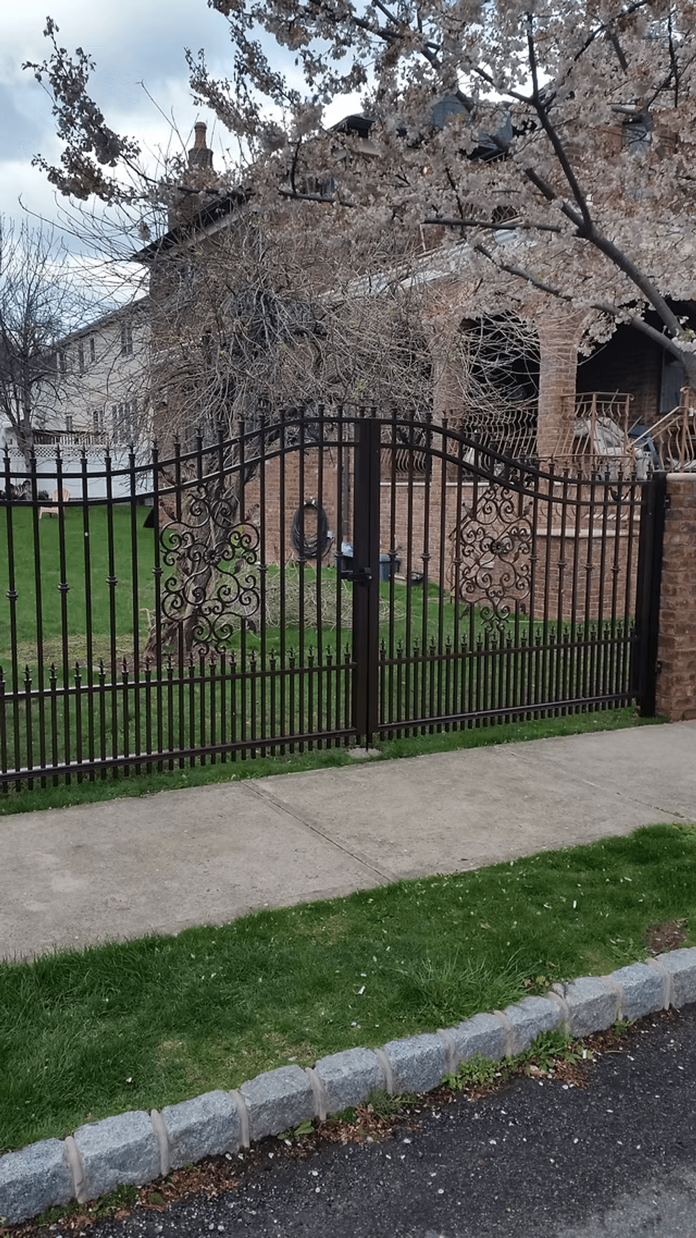 Wrought iron gate with intricate design in front of a brick house and blooming trees.
