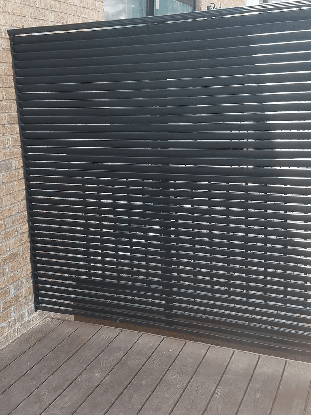 Modern black wooden slatted wall with sunlight casting shadows on the patio.