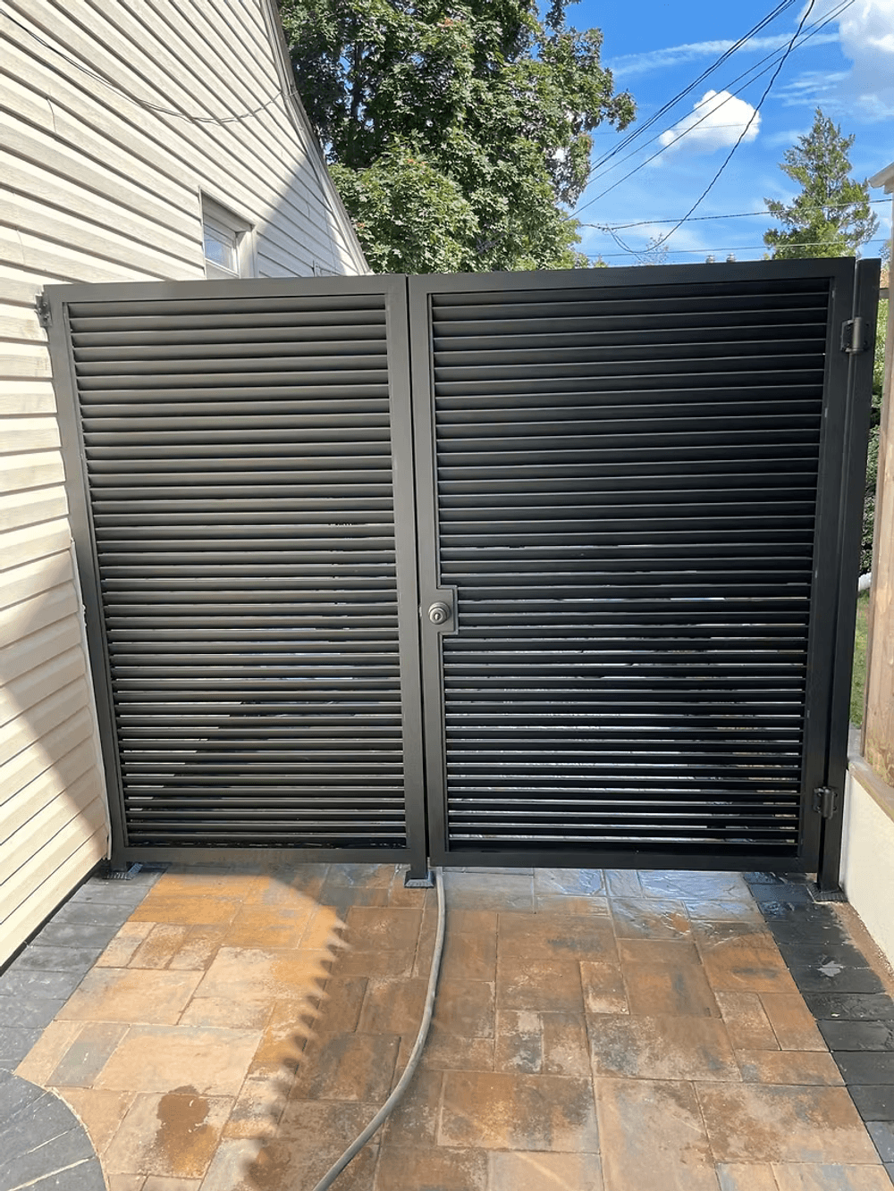 Black horizontal slatted metal gate with a lock, set against a bright blue sky.