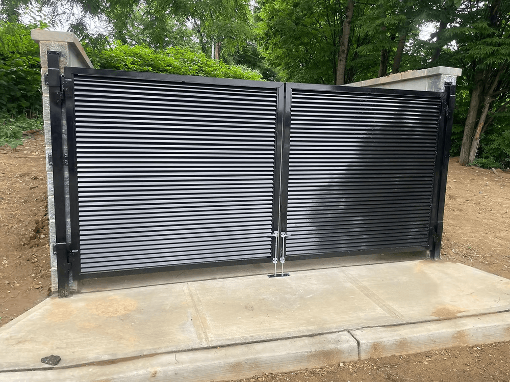Black horizontal slatted gate on a concrete pathway in a lush green setting.