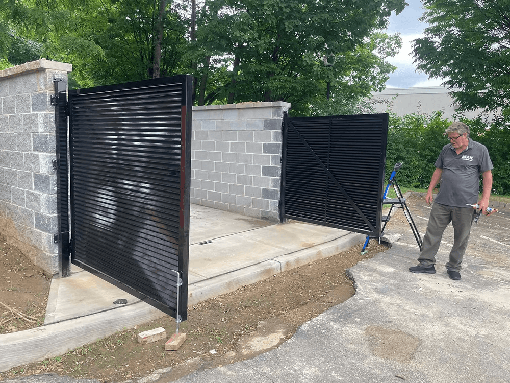 Modern black metal gate installed beside a stone wall, with a man making adjustments.