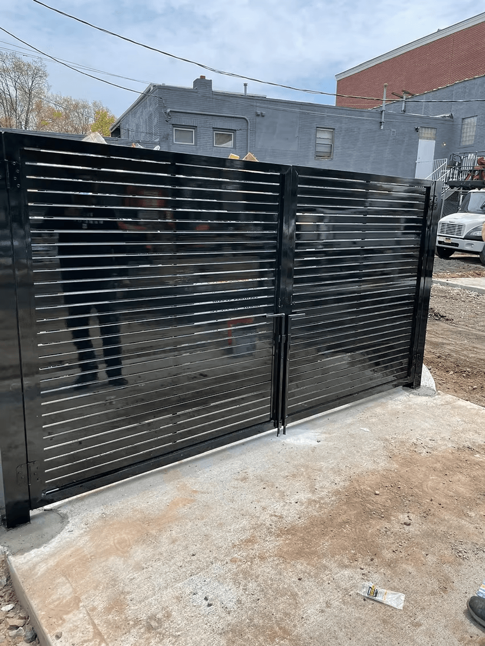 Modern black metal slatted gate with a sleek design on a concrete foundation.