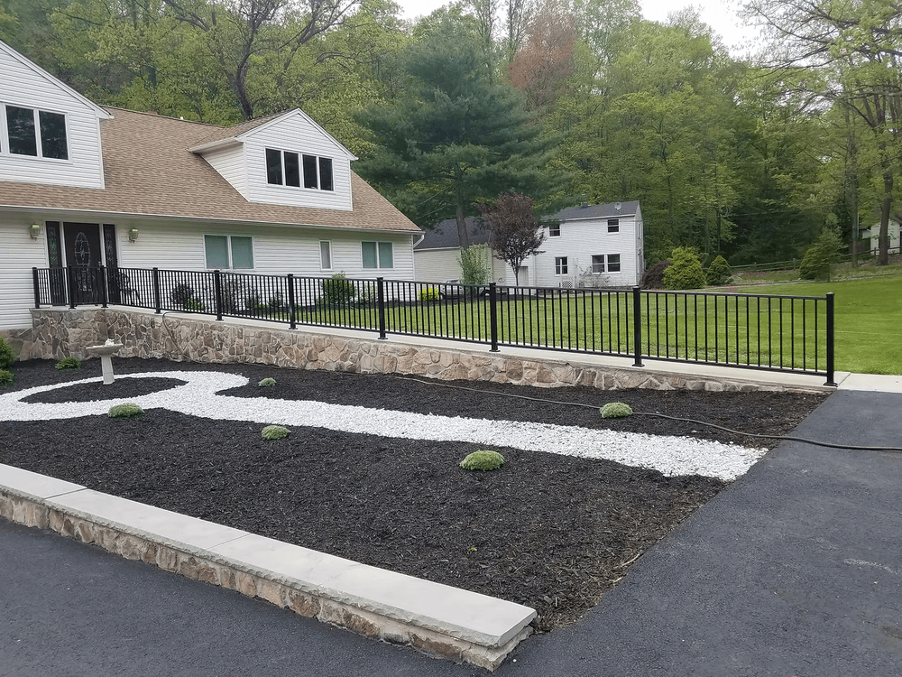 Landscaped front yard featuring stone borders, white gravel path, and black metal railing.