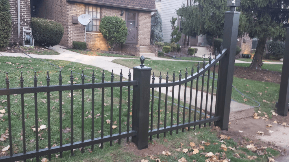 Black wrought iron fence with decorative gate in front of a residential home and landscaped yard.
