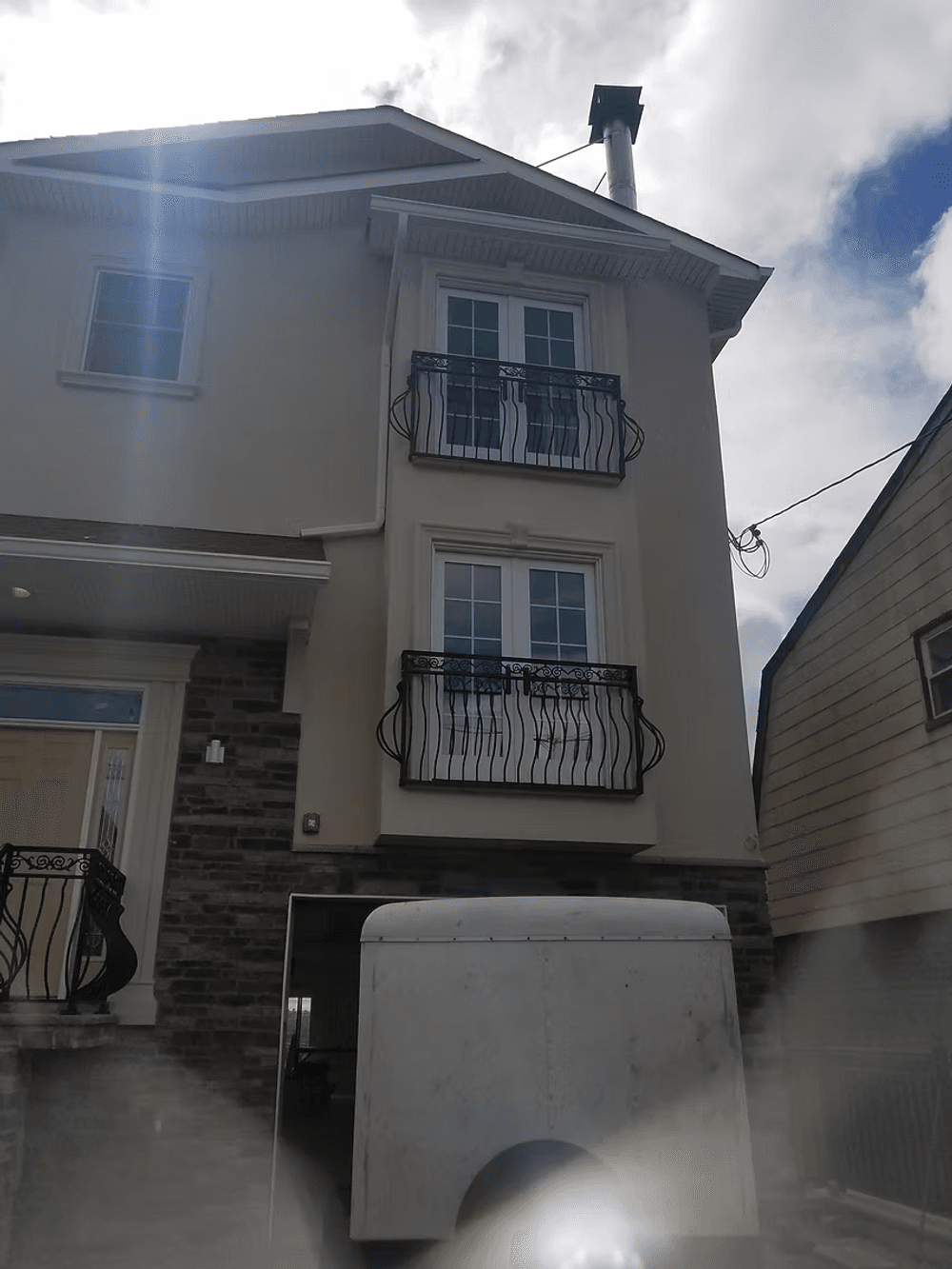 Modern two-story house with decorative balconies and a chimney, featuring stone accents.