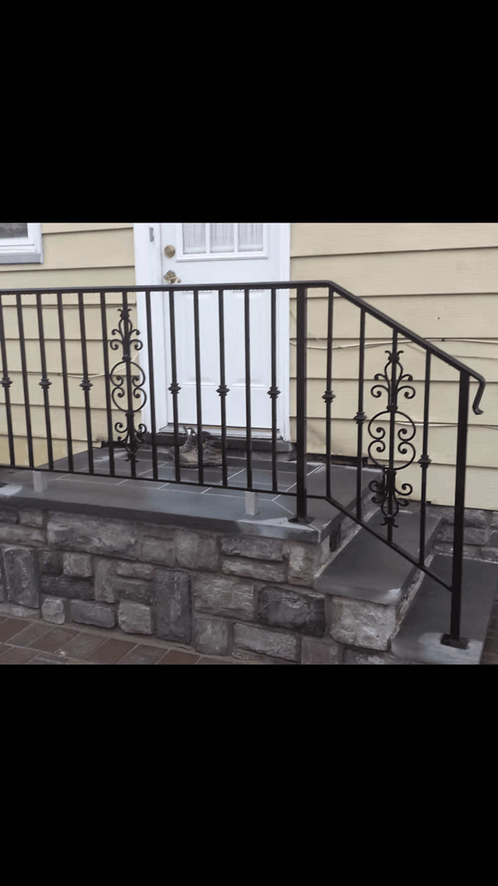 Black wrought iron railing on a stone staircase leading to a front entrance door.