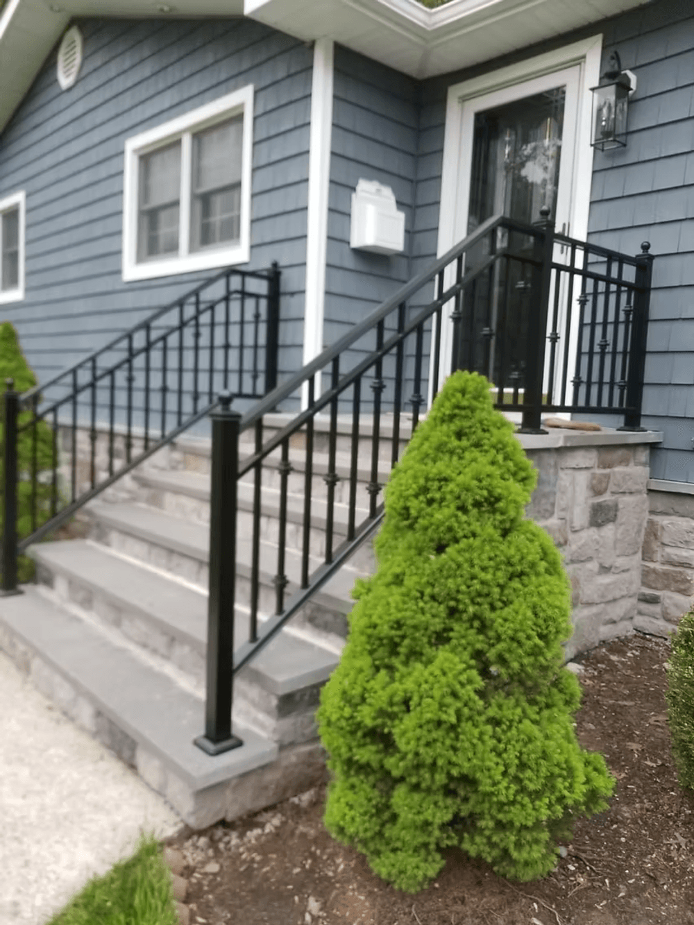 Elegant black metal railing on stone steps leading to a blue home with neatly trimmed shrubs.