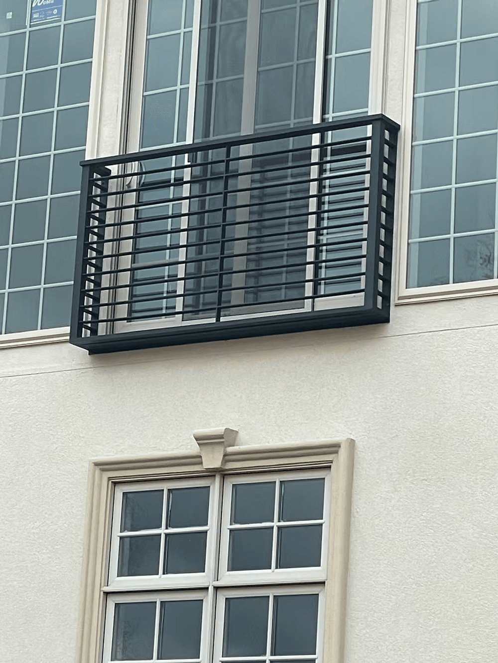 Black metal balcony railing on a modern building with large windows.