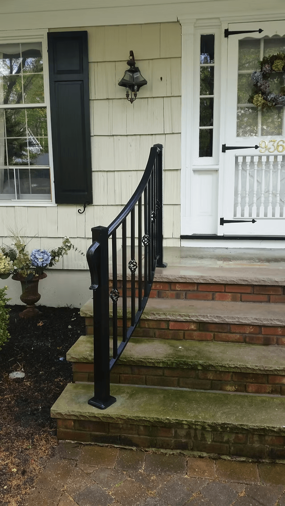 Black metal railing on brick steps leading to a white front door with flower details.