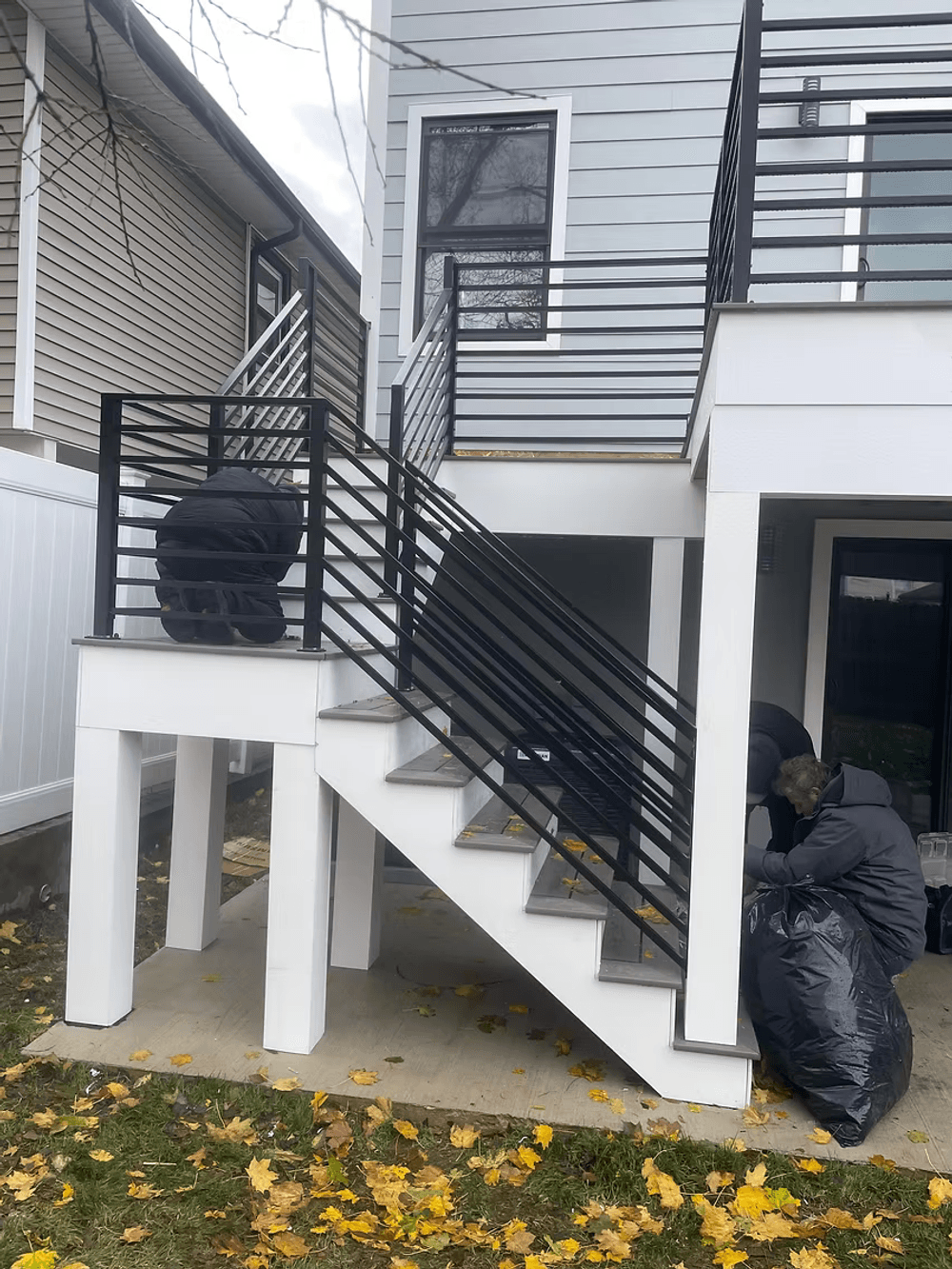 Workers installing modern black railings on outdoor staircase of a two-story house.