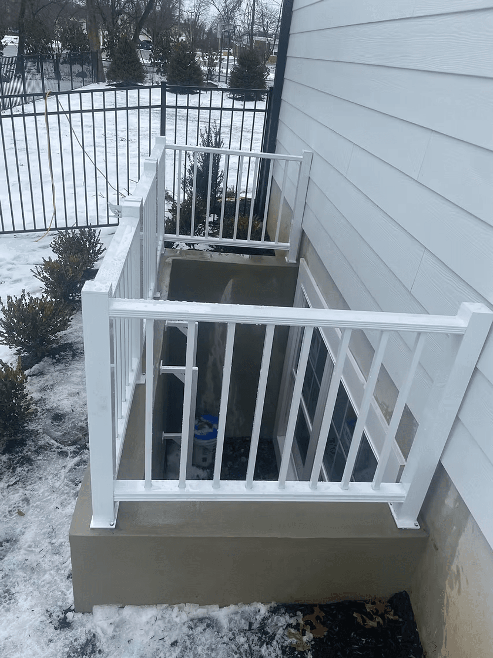 White railing surrounds a small basement entryway on a snowy day, enhancing outdoor safety.