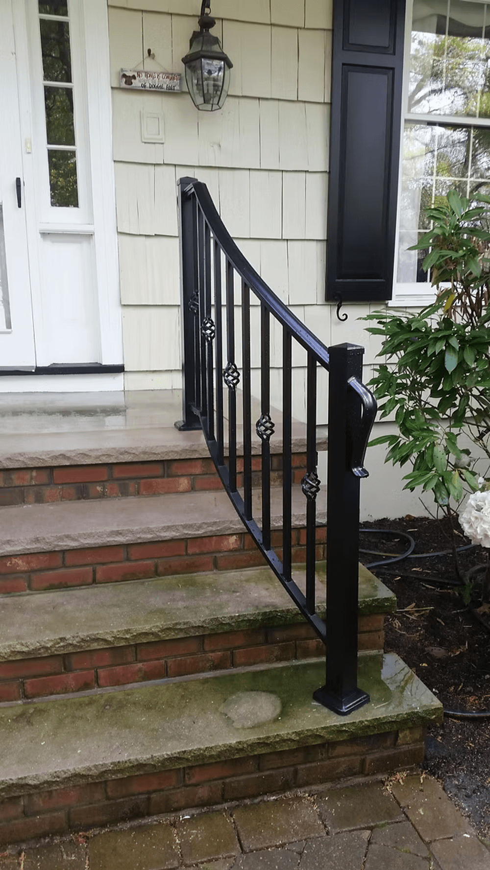 Black wrought iron railing on stone steps leading to a home entrance with landscaping.