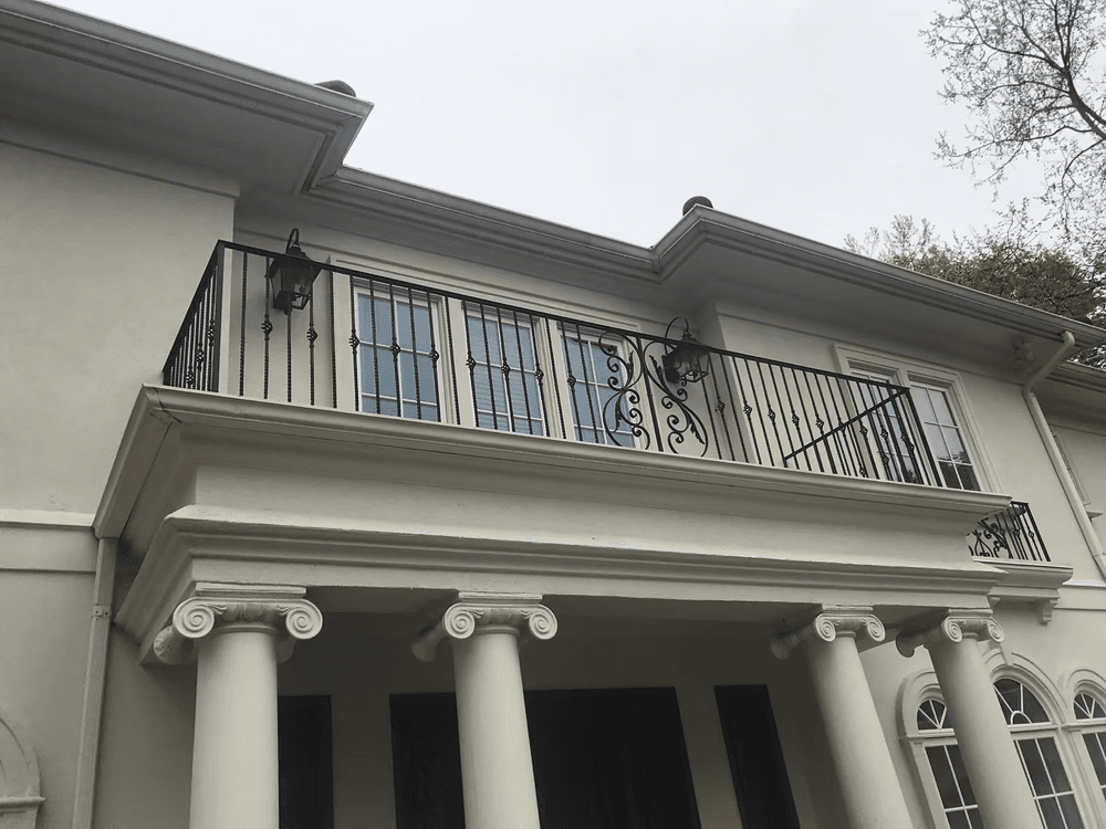 Elegant white house with wrought iron balcony and columns under a cloudy sky.