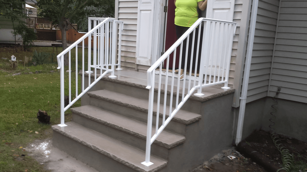 White handrails on concrete steps leading to a home entrance with a person standing nearby.