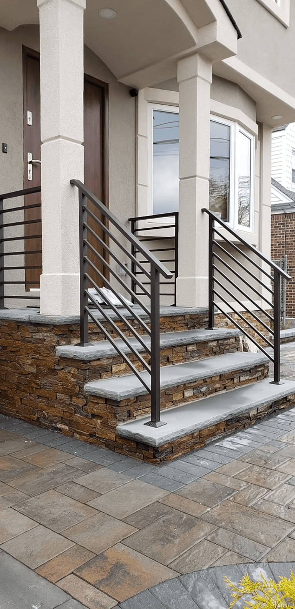Modern home entrance with stone steps, metal railing, and landscaped pathway.