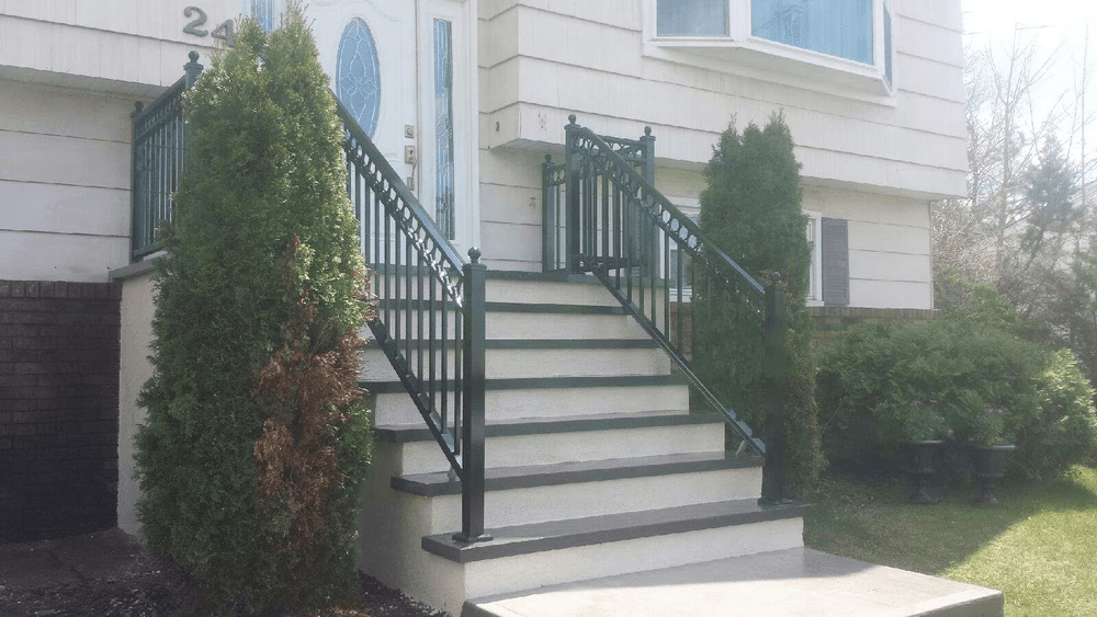 Home entrance featuring a staircase, black railings, and landscaped greenery.