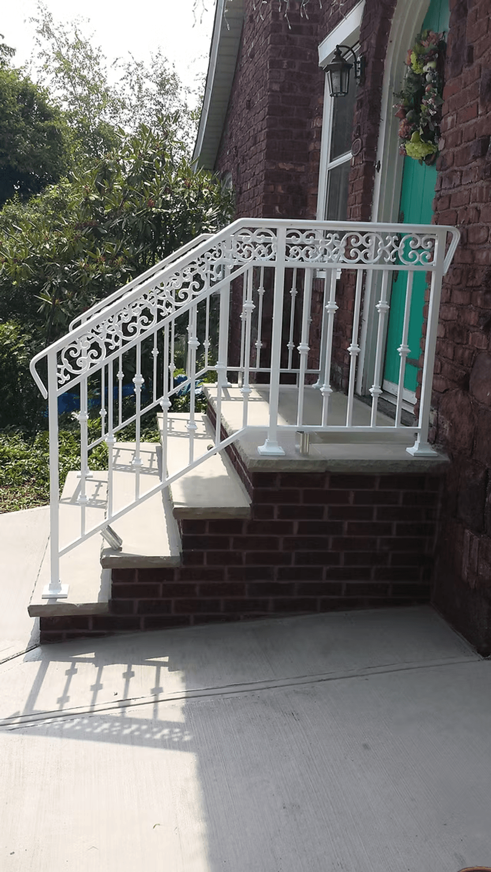 White decorative metal railing on brick steps leading to a green door, featuring sunlight shadows.