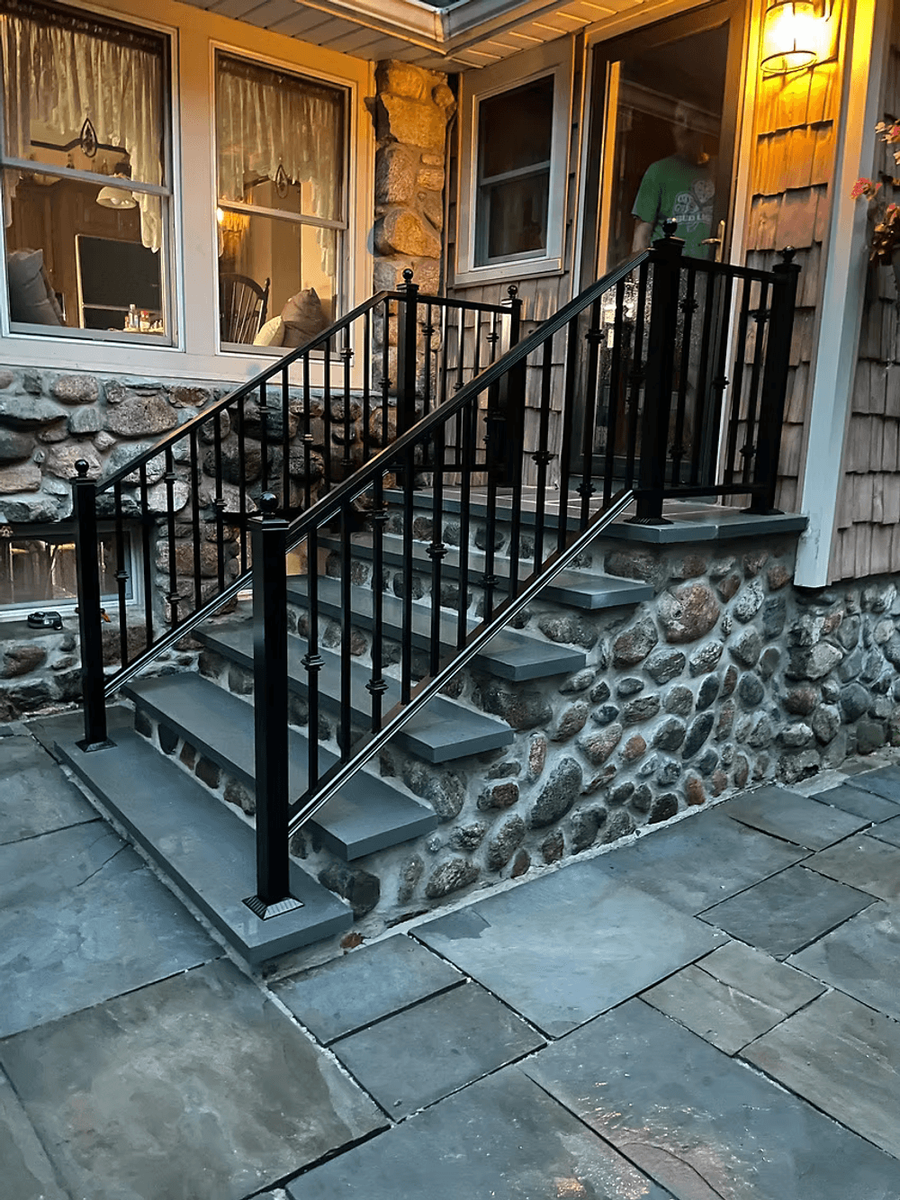 Black wrought iron railing on stone steps leading to a modern home entrance at dusk.