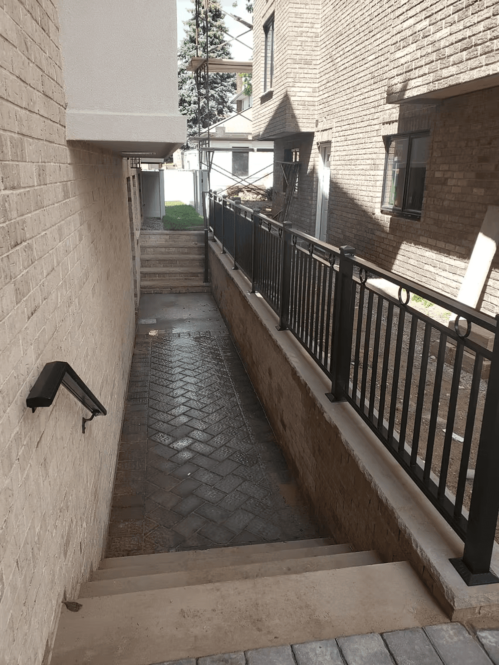 Narrow walkway between brick buildings with metal railing and steps.