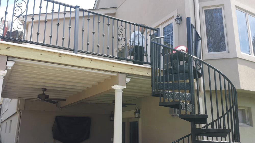 Spiral staircase leading to an upper balcony with railing and outdoor seating area.