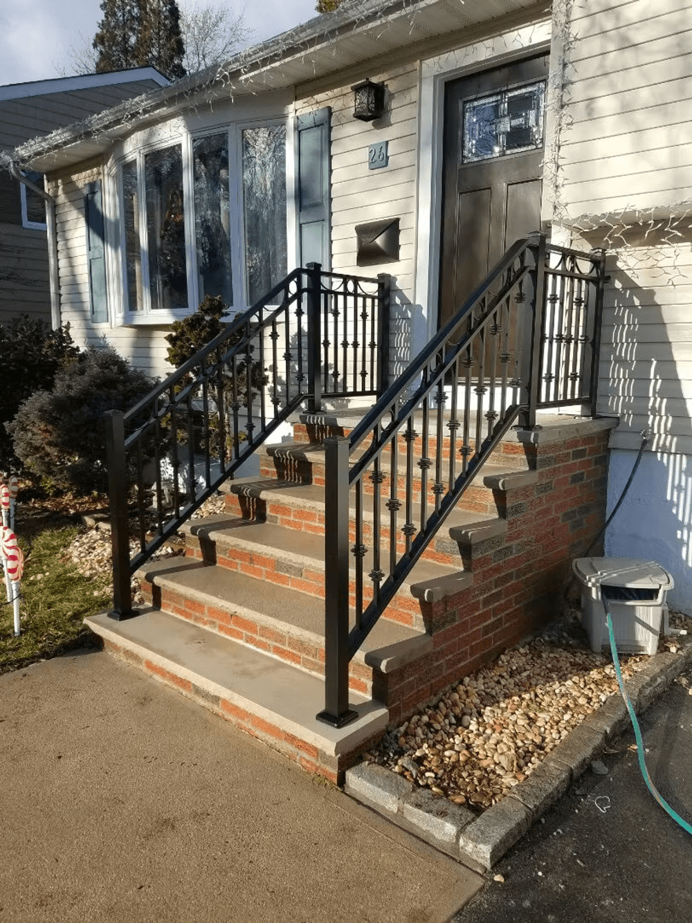 Black metal railing on brick steps leading to a front door with holiday decorations.