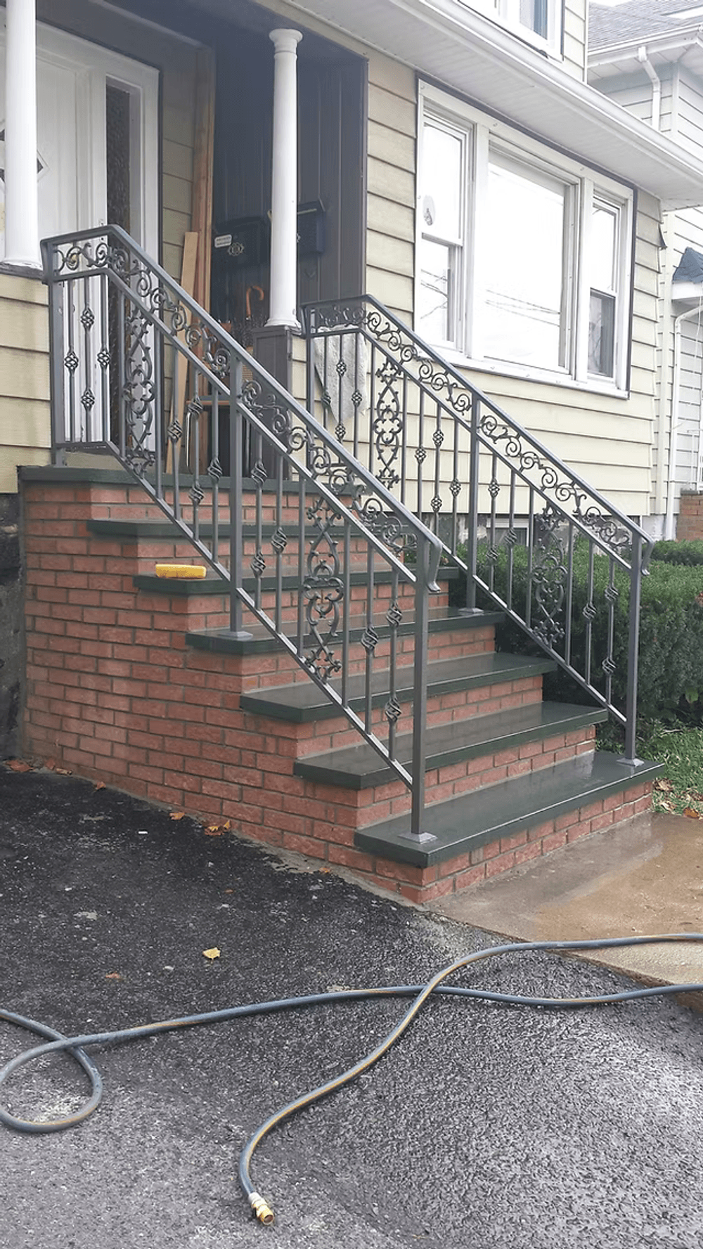 Brick staircase with decorative metal railing and green shrubs, leading to front entrance.