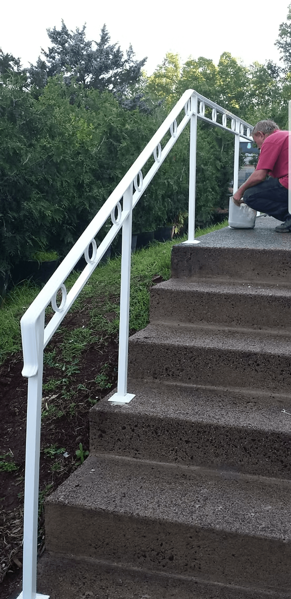 Man working on white metal railing installation on outdoor concrete stairs.