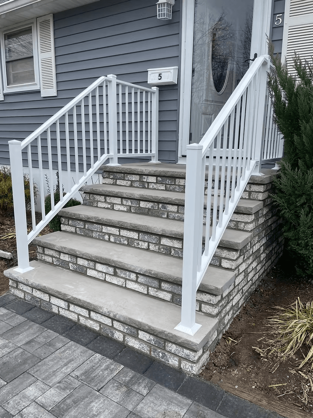 White railing stairs leading to a front door, featuring brick and concrete design.