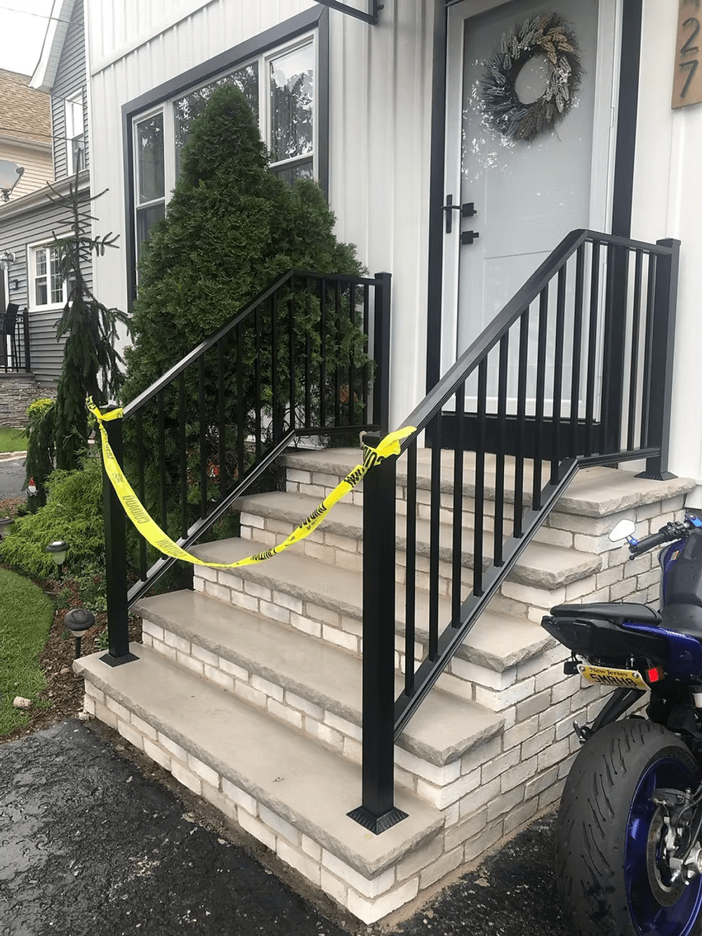 Black railing with caution tape blocking stairs leading to a house entrance.