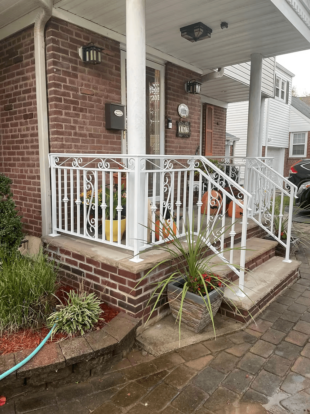 White wrought iron handrail on brick porch with colorful flower pots and greenery.