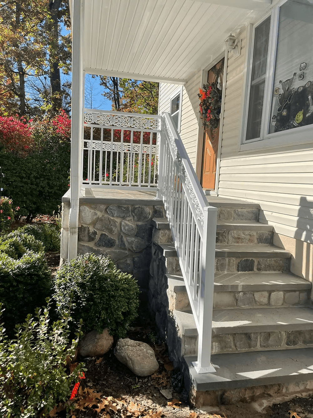 White railing and steps lead to a front porch surrounded by vibrant fall foliage.