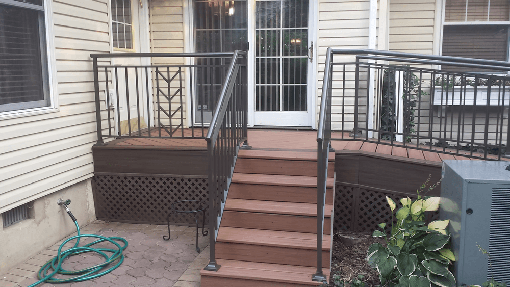 Composite deck with handrails and steps, leading to a door, surrounded by greenery.