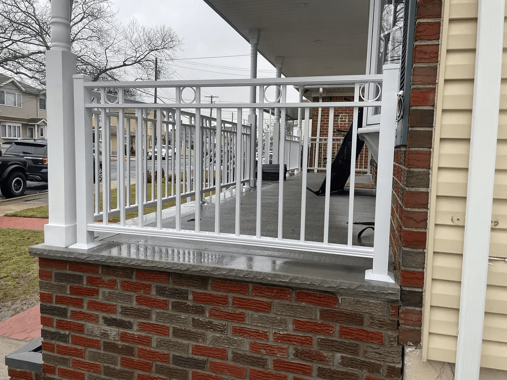 White railing on a brick porch with a view of the neighborhood in a cloudy setting.