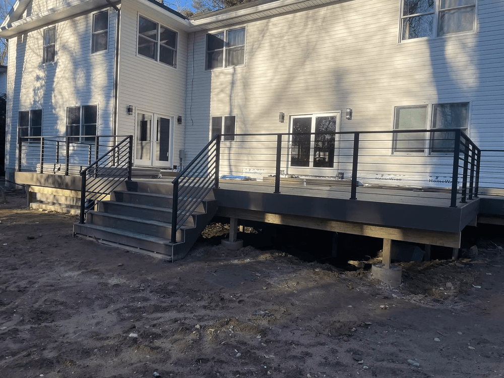 Newly constructed outdoor deck with black railing and stairs, attached to a modern house.