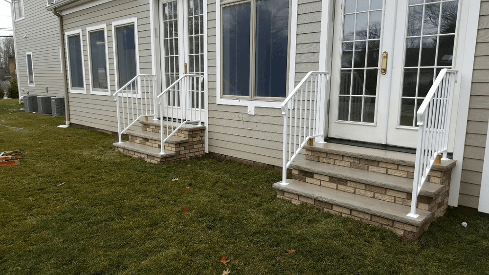 White metal railings on stone steps leading to modern home entrance with large windows.